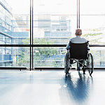 Senior Man in Wheelchair looking out of a window in a hospital corridor.