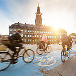 Blurred people going by bike in Copenhagen, with Christiansborg palace on background. 