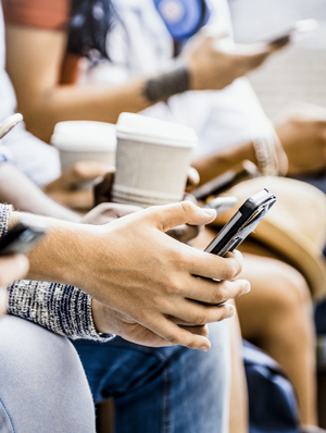 Close-up of people's hands using smartphones and holding paper coffee cups.