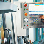 Close-up rear view of a control room at a modern industrial production site where a control operator monitors plant operation processes on a computer.