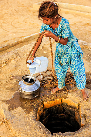 A young Indian girl fills a metal container with water from a well.