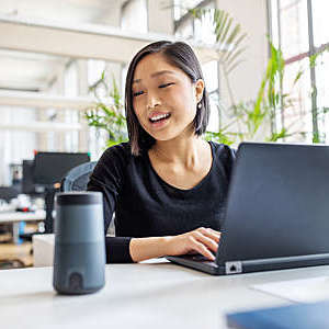 Asian woman talking to a virtual assistant, at her desk.