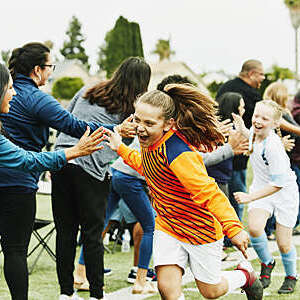 Young female soccer goalie high-fives parents on the sidelines after a soccer game.