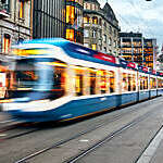 Blurred view of blue and white tram speeding across a city centre.