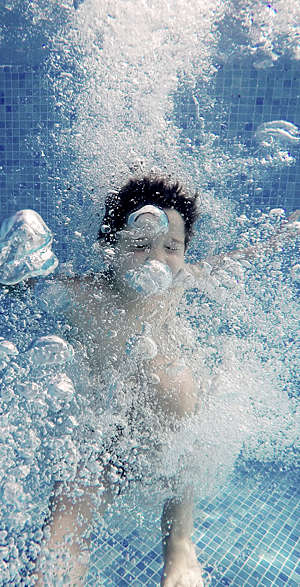Underwater view of a little boy immersed in bubbles after a jump in the pool.