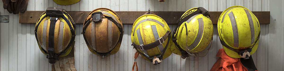 Row of yellow safety helmets hanging from a wooden rack at a mining site.