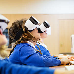 Young children, open-mouthed with excitement as they use virtual reality goggles in a computer lab at school.