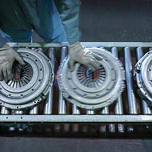 Overhead view of worker’s hands moving clutch pressure plates down the production line in an industrial clutch factory.