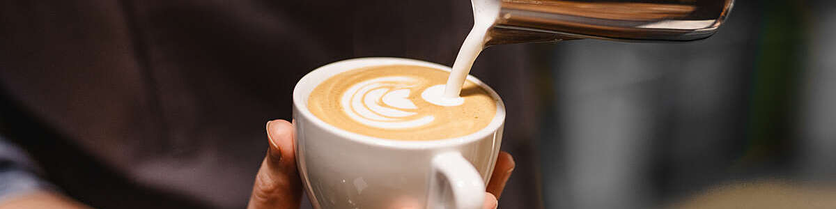 Close up view of the hands of a barista preparing a coffee by drawing a flower with milk.