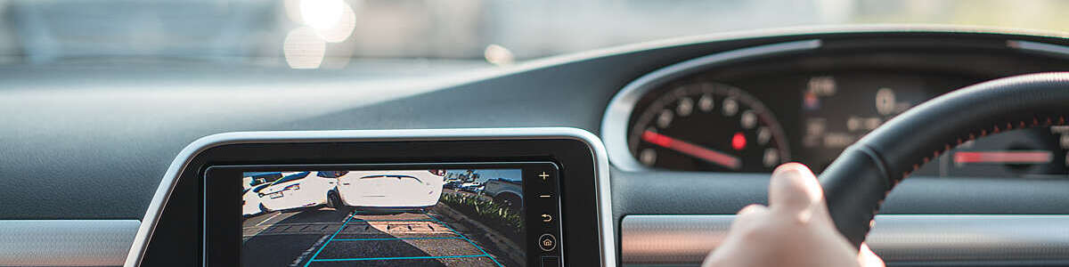 Close-up of rear-area video camera on car dashboard, with view of driver’s hand on steering wheel.