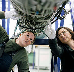 Two female mechanics examine an open jet engine in an aircraft hangar.