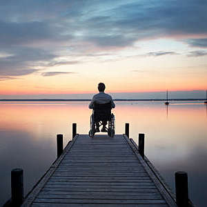 Senior man sitting in wheelchair at the end of lakeside jetty watching majestic cloudscape at dusk